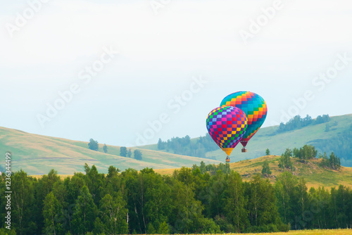 Obraz na płótnie Colorful hot air balloons flying over the green hills and trees at sunset. w salonie