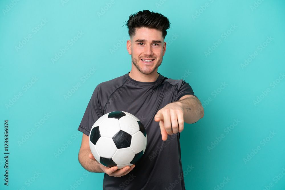 Young caucasian man isolated on blue background with soccer ball and pointing to the front Young caucasian man isolated on blue background with soccer ball and pointing to the front