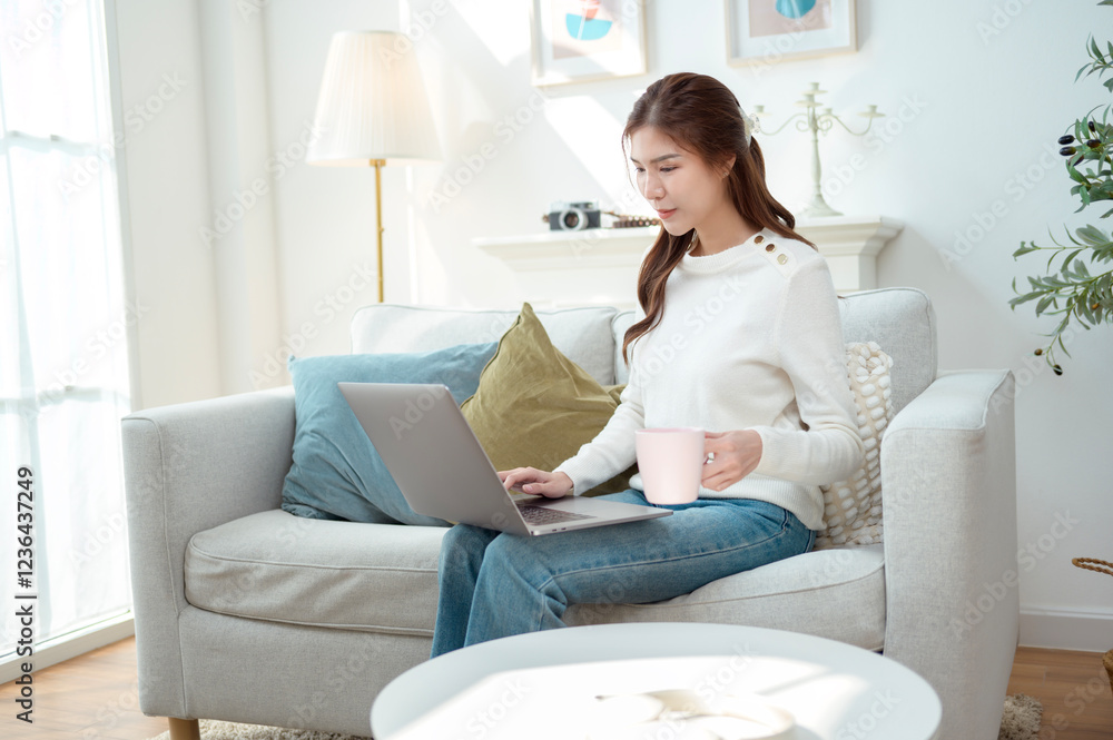 Young Woman Enjoys Working on a Laptop While Sipping Coffee in a Cozy Living Room Setting Young Woman Enjoys Working on a Laptop While Sipping Coffee in a Cozy Living Room Setting