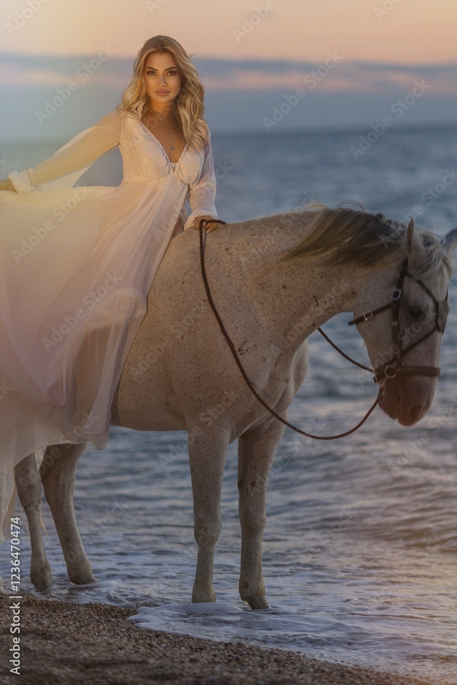 Young long-haired woman in a white dress riding a white horse against a seascape