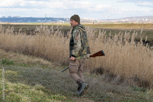 Mature hunter man holding a shotgun and walking through a field photo