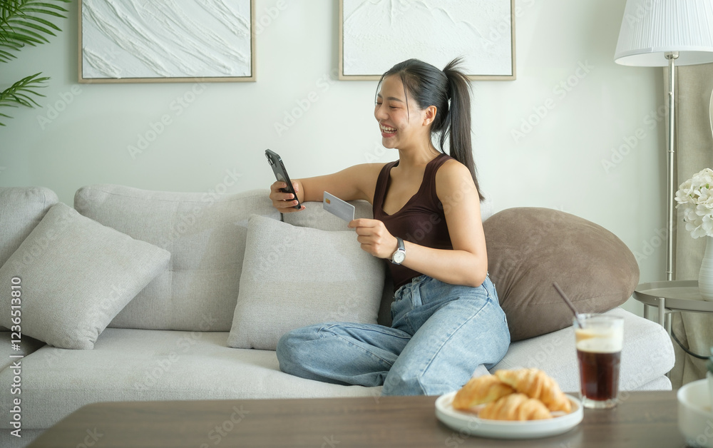 A smiling woman sitting on a comfortable sofa, holding her smartphone and a credit card, enjoying a relaxed online shopping experience. A smiling woman sitting on a comfortable sofa, holding her smartphone and a credit card, enjoying a relaxed online shopping experience.