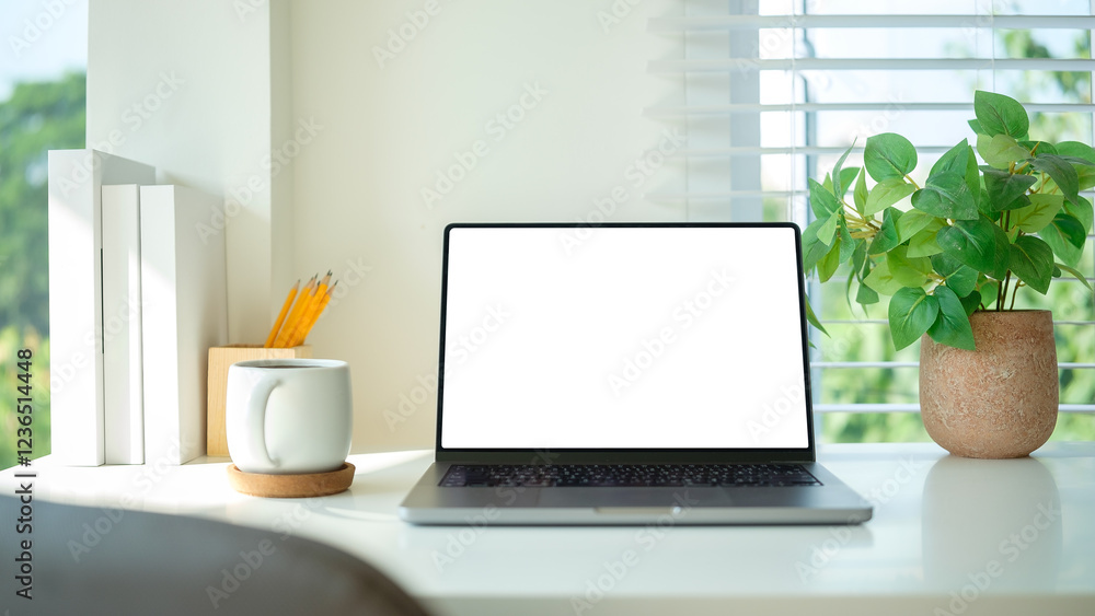 Fototapeta premium White desk with a laptop, coffee mug, green potted plant and books.