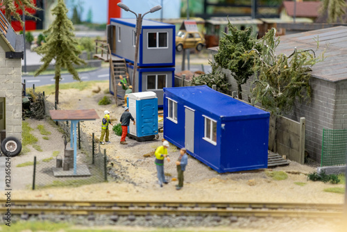 construction workers setting up portable toilets and modular blue office cabins at a construction site near a railway