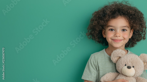 cheerful child with curly hair holding teddy bear against green background