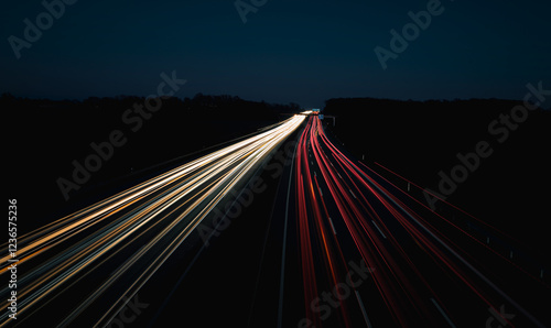 A long-exposure photograph capturing highway traffic at night, creating stunning light trails. The image shows bright white and red streaks from vehicle headlights and taillights against a dark backgr