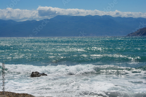 A view of the Adriatic Sea from beach in Baska on Island Krk featuring waves crashing against the shore with the Velebit mountain range in the background photo