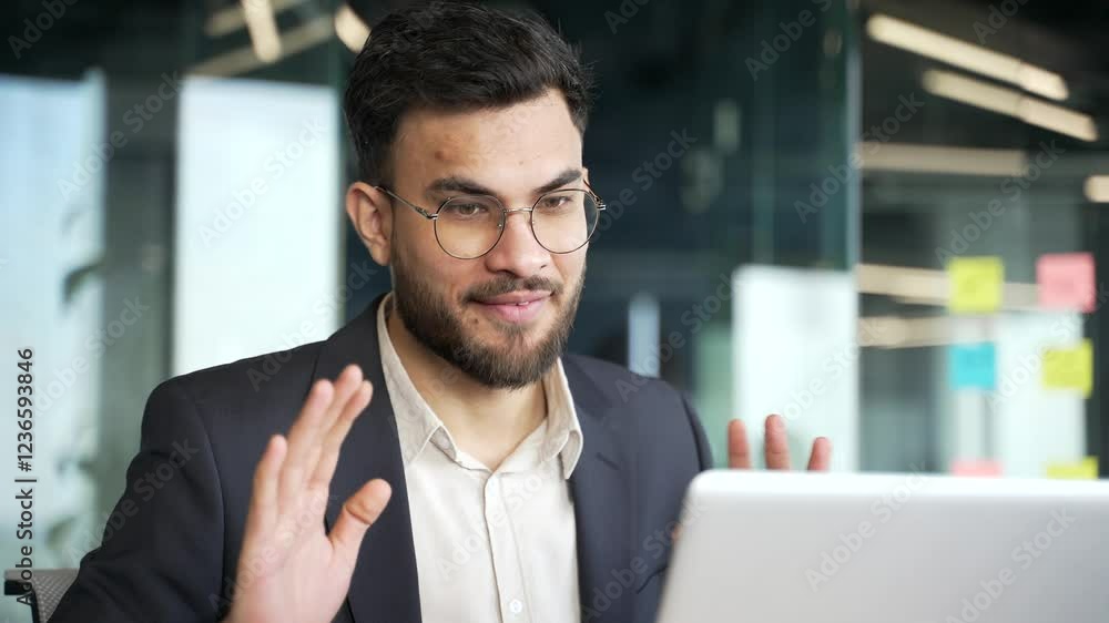 Smiling businessman in a formal suit talking on a video call using a laptop in office. A friendly employee communicates with a colleague. Coach speaks remotely at an online training session. Close up Smiling businessman in a formal suit talking on a video call using a laptop in office. A friendly employee communicates with a colleague. Coach speaks remotely at an online training session. Close up
