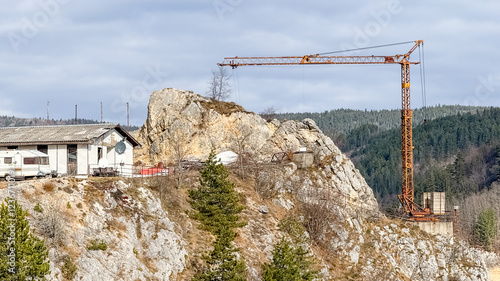 A construction crane towers over a rocky outcrop near a remote house, illustrating rural development challenges in rugged landscapes