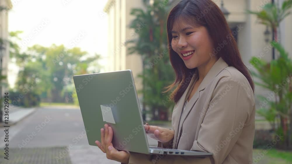 Asian businesswoman standing outdoors, using laptop computer device in modern city. Asian businesswoman standing outdoors, using laptop computer device in modern city.