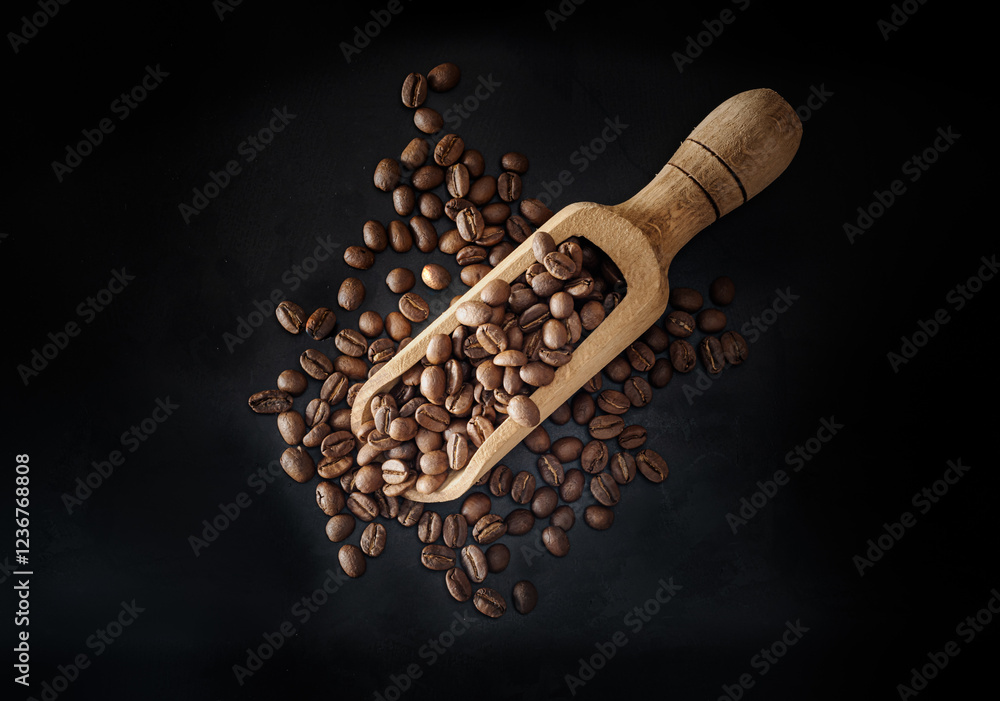 Top view of Roasted coffee beans on a rich textured surface in Wooden coffee scoop on dark background. Enjoy your morning coffee for living, use it as your Space for text, Design, Wallpaper and Poster