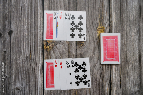 Two hands of playing cards laid out on a rustic wooden surface during a casual game night. The cards include kings, aces, and various numbered cards, inviting friendly competition photo