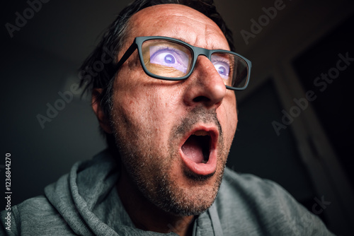 Surprised and shocked man looking at computer screen while browsing internet or social media photo