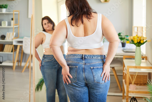 Pleasant obese woman posing in front of mirror at home wearing top, jeans, chubby overweight plus size big fat fit lady thinking about progress in weight loss after sport, dieting, looking, planning