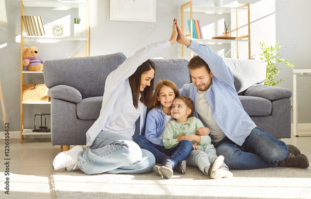 Portrait of happy young smiling parents making roof from hands above their little children sitting on floor in living room at home. Insurance, mortgage, safety and family protection concept. Portrait of happy young smiling parents making roof from hands above their little children sitting on floor in living room at home. Insurance, mortgage, safety and family protection concept.