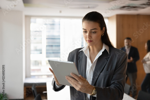 Serious young manager woman preparing electronic report for presentation, using tablet computer in office meeting room, touching screen, using web service for analysis job