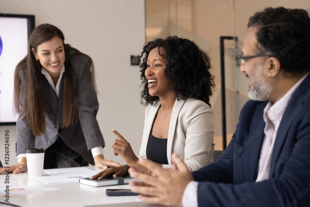 Positive young African American manager woman offering creative ideas for project at business team meeting, talking to diverse colleagues at office table, speaking, smiling, laughing Positive young African American manager woman offering creative ideas for project at business team meeting, talking to diverse colleagues at office table, speaking, smiling, laughing