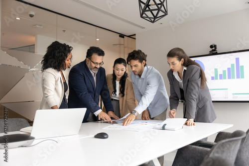 Diverse different aged business team of serious colleagues analyzing financial reports, marketing research results together, bending over meeting table, reviewing paper documents photo