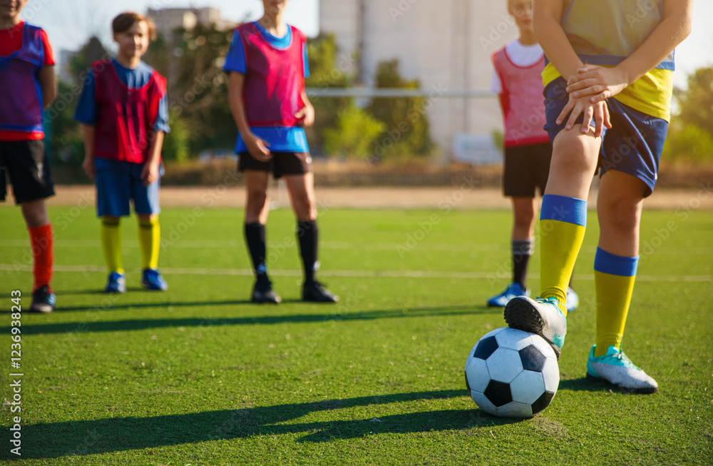 A group of young soccer players in colorful jerseys and shorts, practicing on a green field. One child is about to kick a soccer ball, while others stand ready for their turn. A group of young soccer players in colorful jerseys and shorts, practicing on a green field. One child is about to kick a soccer ball, while others stand ready for their turn.