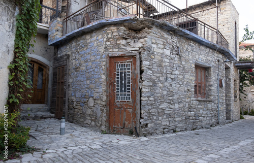 Old weathered stone house with red door and balcony in traditional village photo