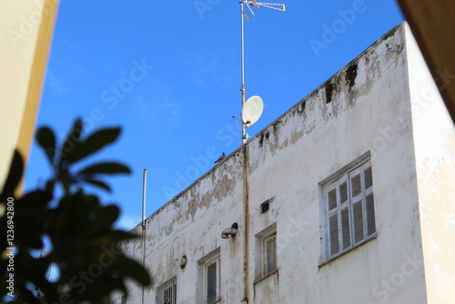 Weathered Urban Building with Satellite Dish and Rooftop Antenna Against a Blue Sky