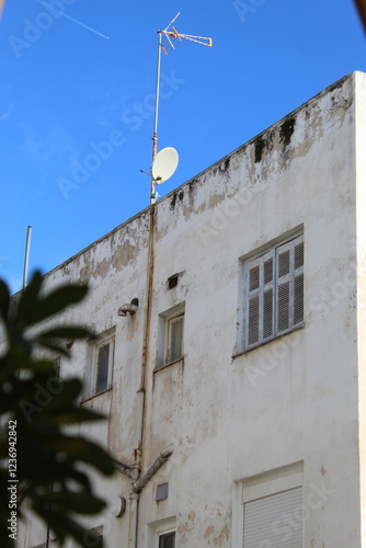 Weathered Urban Building with Satellite Dish and Rooftop Antenna Against a Blue Sky