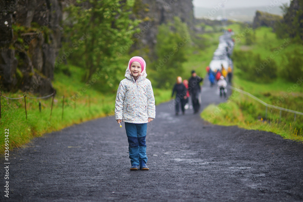 Fototapeta premium Adorable preschooler girl in Thingvellir national park in Iceland with black volcanic rocks and green plants.