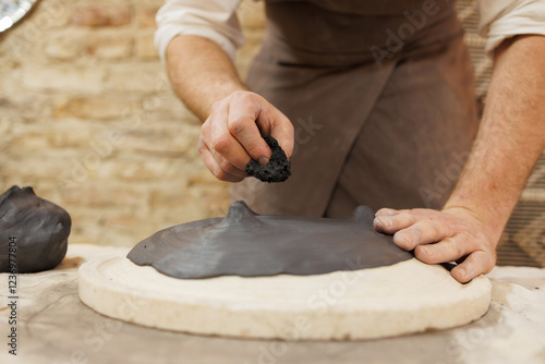 Cropped shot of artisan holding sponge near clay plate in pottery studio