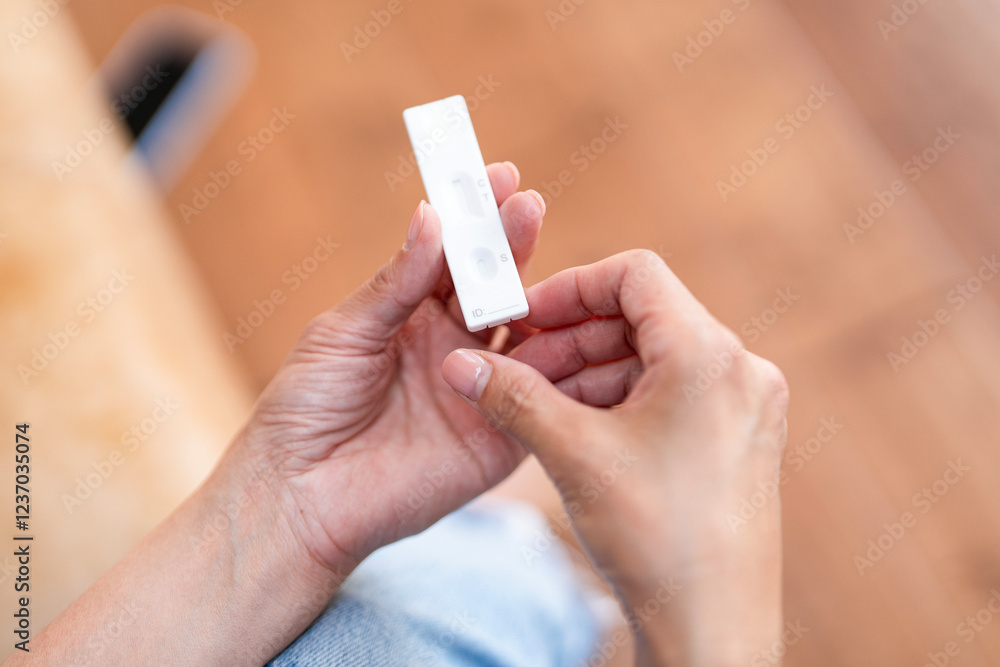 Hands holding COVID test while sitting on a couch in a cozy living area Hands holding COVID test while sitting on a couch in a cozy living area