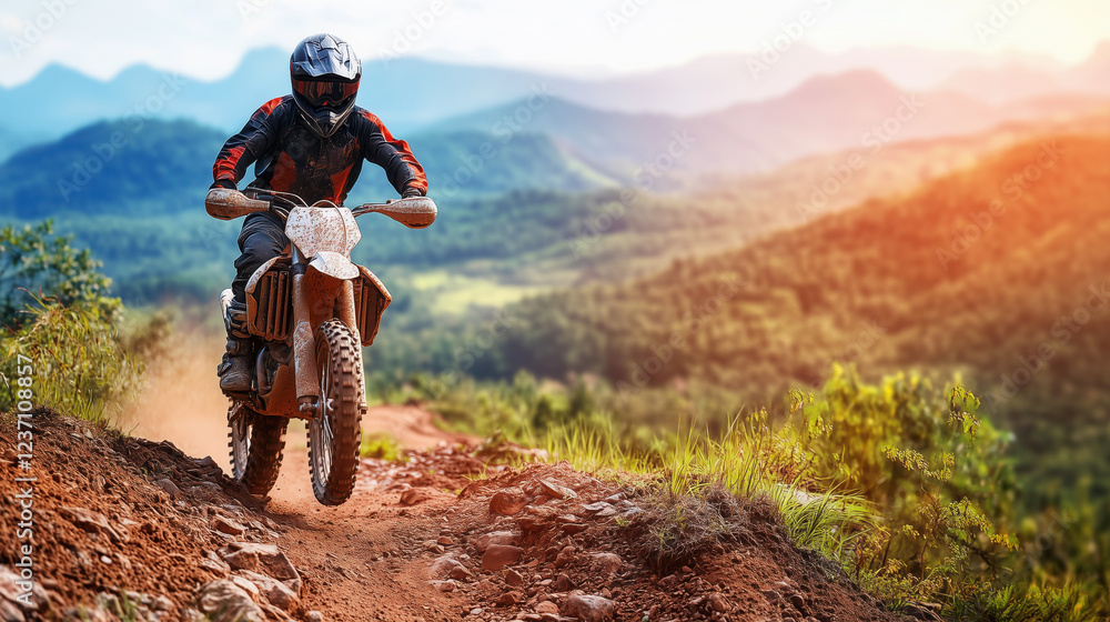 Naklejka premium Biker in Off-Road Gear Climbing a Steep Hill on a Rugged Dirt Trail, with a Blurred Mountain Range Creating a Dramatic Backdrop for an Adventurous Ascent