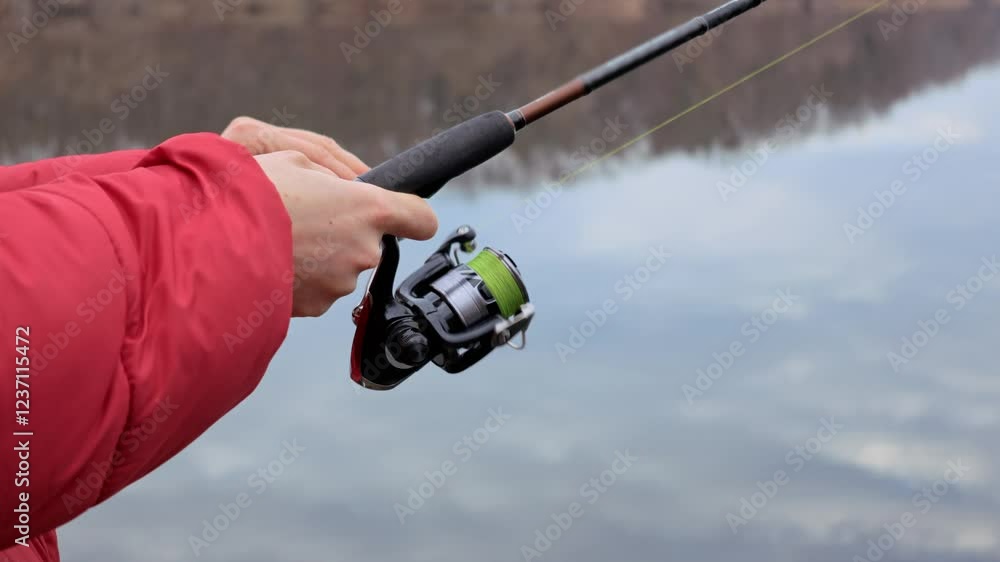 Hands spinning a spinning reel, close-up. River fishing, catching predatory fish with a spinning rod Hands spinning a spinning reel, close-up. River fishing, catching predatory fish with a spinning rod