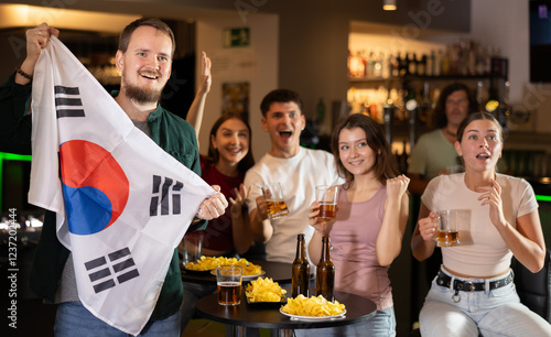 Football fans gesturing emotionally after goal scored by favorite team while watching championship match on TV in sports bar on background with North Korea flag photo