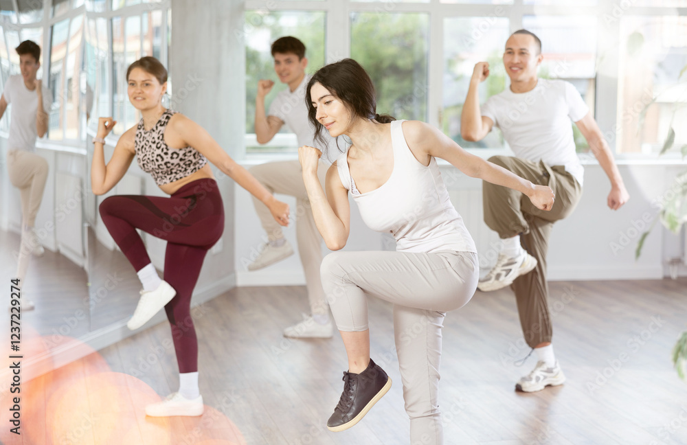 Fototapeta premium Sporty smiling young brunette practicing rhythmic aerobics during group workout in fitness studio. Active lifestyle concept