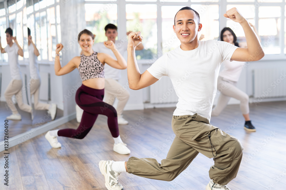Fototapeta premium Positive woman and man engaged in dancing in group practices energetic swing in a dance studio