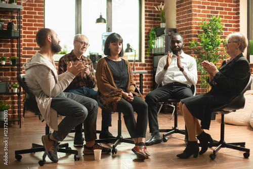 Supportive community clapping for young woman during aa meeting in brick wall office. Caucasian lady sitting in middle of circle being celebrated for mental health recovery at group therapy session. photo