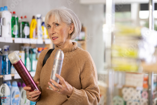 Attentive old woman reviewing hair sprays to buy in shop with large stock