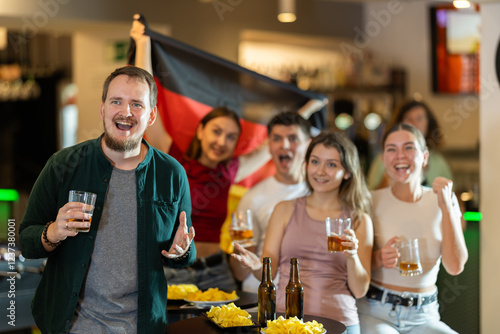 Group of friends fans watching match cheering with German flag in bar photo