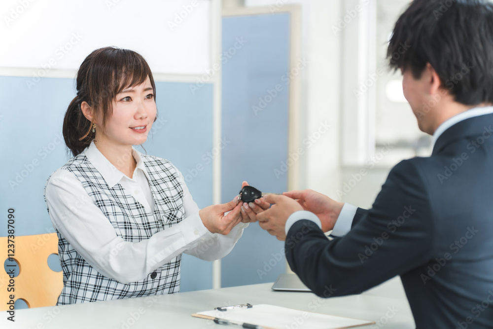 Fototapeta premium 受付で車の鍵の受け渡しをする女性スタッフと顧客の男性 