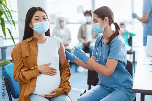 Vaccination In Pregnancy. Pregnant Asian Woman Getting Vaccinated For flu Prevention, Nurse Giving Vaccine Shot Against Coronavirus Injecting Mother-To-Be In Clinic, Wearing Face Masks And Gloves