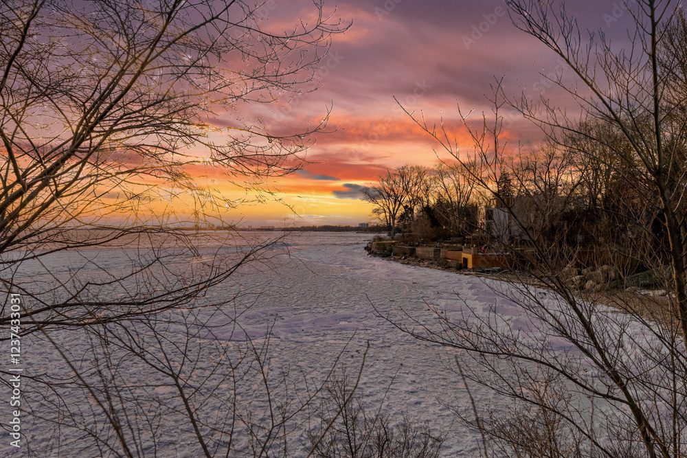 Winter sunset over a frozen lake, with bare trees framing the scene. Winter sunset over a frozen lake, with bare trees framing the scene.