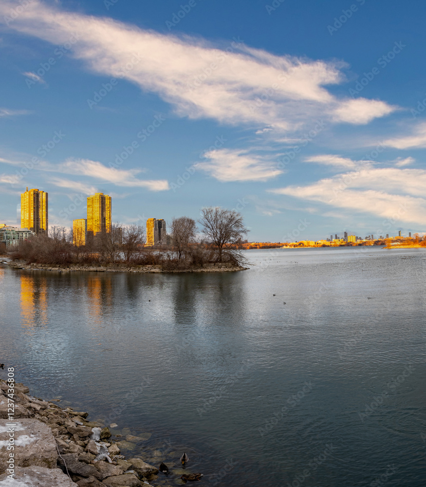 Obraz premium City skyline reflected in calm lake waters, winter trees.