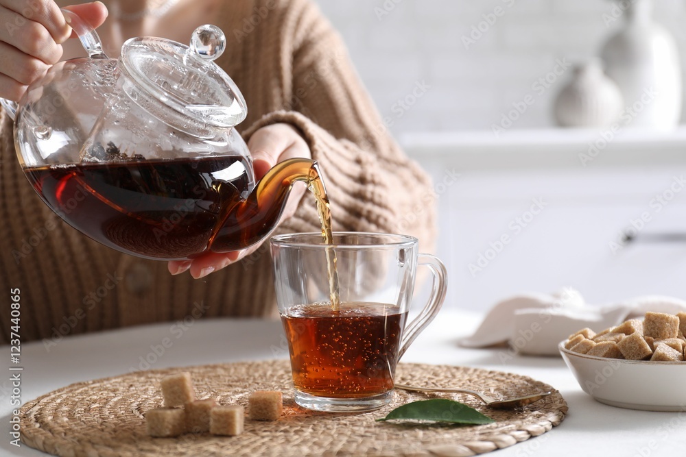 Woman pouring hot black tea into cup at white table, closeup Woman pouring hot black tea into cup at white table, closeup