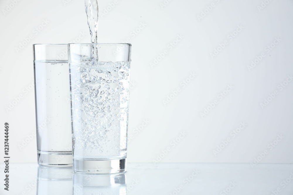 Pouring refreshing soda water into glasses on light background, closeup. Space for text Pouring refreshing soda water into glasses on light background, closeup. Space for text