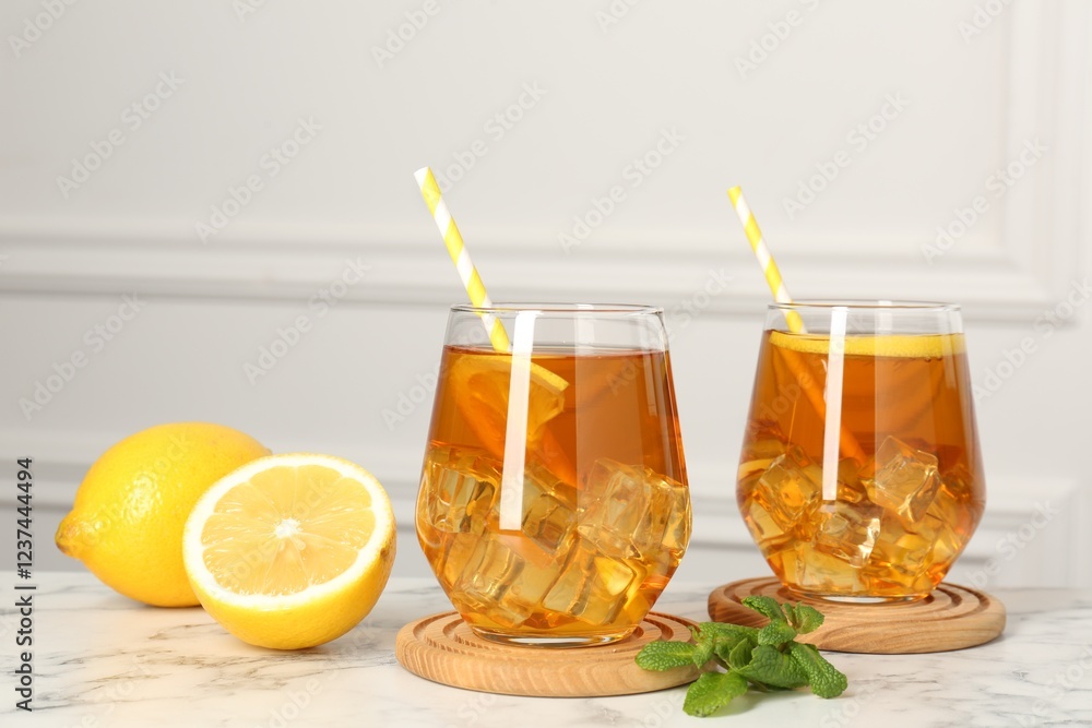Refreshing iced tea with slices of lemon, mint and drinking straws on white marble table Refreshing iced tea with slices of lemon, mint and drinking straws on white marble table