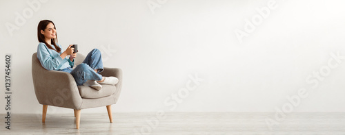Принти на полотні Cheerful young woman drinking aromatic coffee while chilling in comfy armchair against white wall, panorama with blank space
