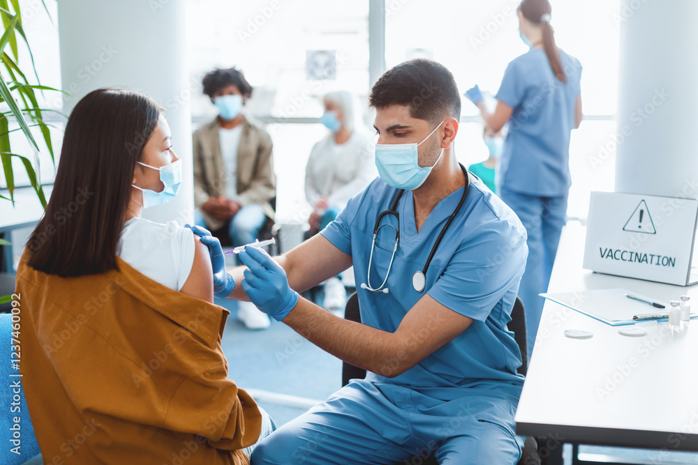 Obraz premium Mass Immunization, Prevention Procedure Concept. Young Asian Lady In Surgical Mask Receiving Intramuscular Injection In Arm Getting Shot In Soulder During Doctor's Appointment In Medical Centre