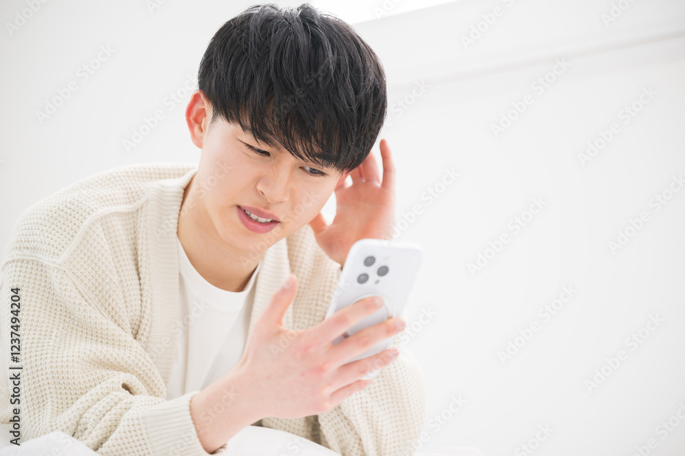 Close-up of a young 20-something male with a troubled, lost, and distressed expression lying face down looking at his phone. Close-up of a young 20-something male with a troubled, lost, and distressed expression lying face down looking at his phone.