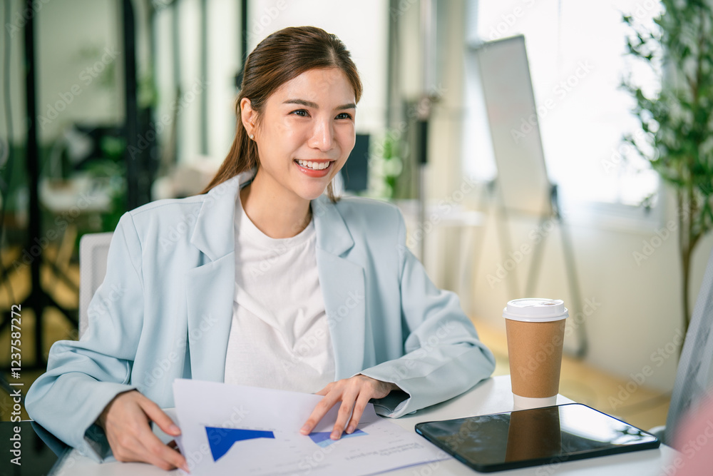 A smiling woman in a light blazer sits at a table with documents and a coffee cup, engaged in a discussion in a bright office environment. A smiling woman in a light blazer sits at a table with documents and a coffee cup, engaged in a discussion in a bright office environment.
