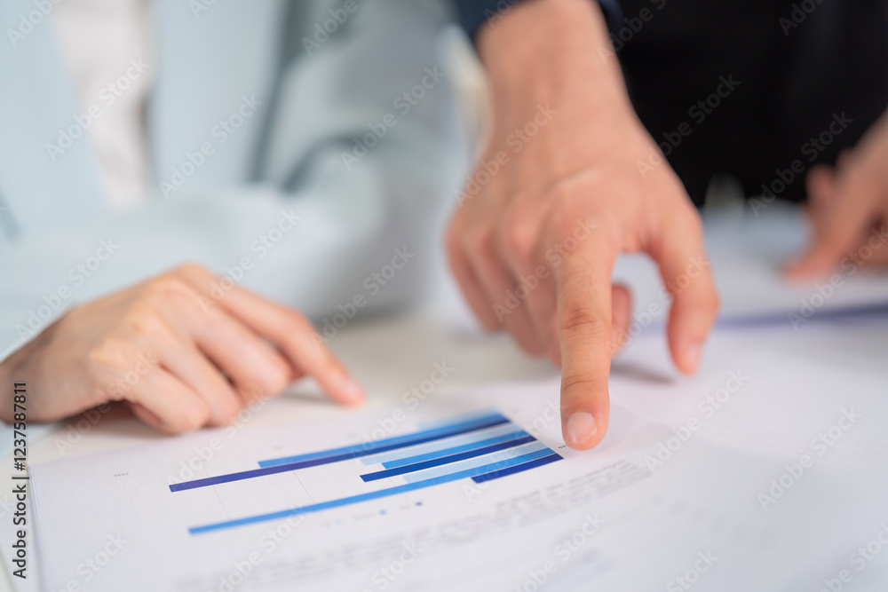 Two hands point at a business report with graphs, indicating teamwork and analysis in a professional setting. Two hands point at a business report with graphs, indicating teamwork and analysis in a professional setting.