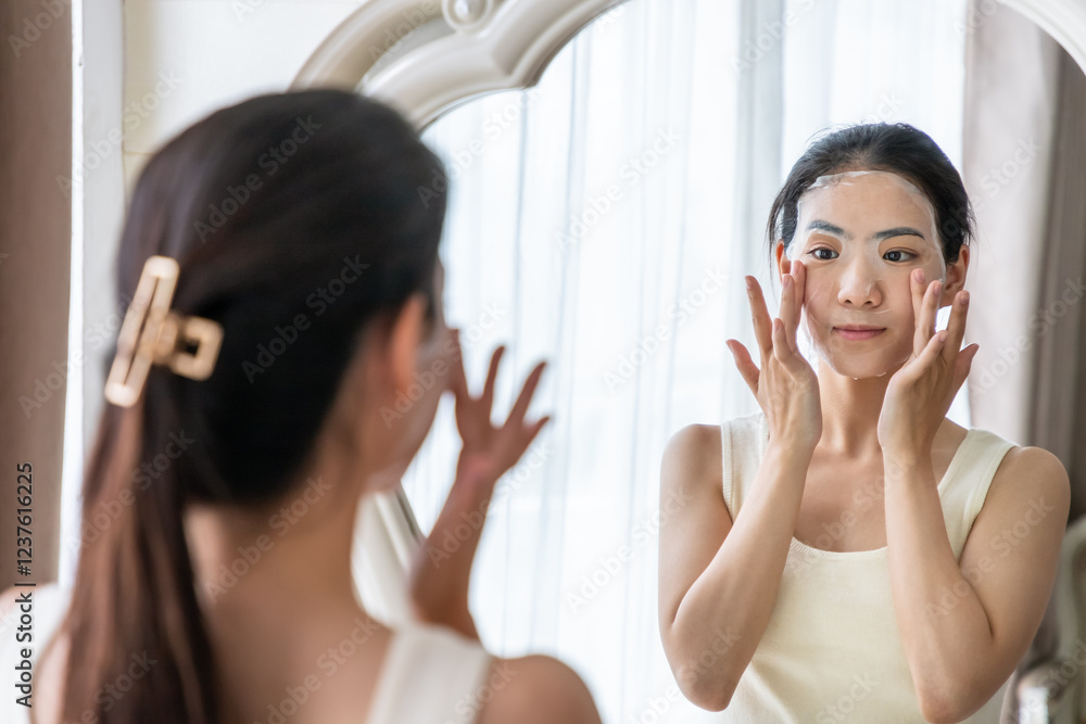 Young Asian woman applying facial mask in front of mirror for skincare routine Young Asian woman applying facial mask in front of mirror for skincare routine